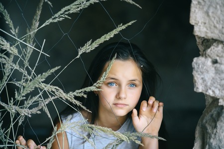 Young girl with adorable blue eyes, long hair, beauty. Little child look through metal mesh. Beauty, look, hairstyle. Childhood, youth concept.の写真素材