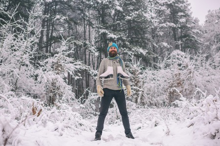 Winter sport and rest, Christmas. Bearded man with skates in snowy forest. skincare and beard care in winter. Temperature, freezing, cold snap, snowfall. Man in thermal jacket, beard warm in winter.の写真素材