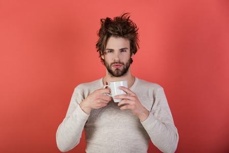 Cold and flu, single. Man with disheveled hair drink mulled wine. Insomnia, refreshment and energy. Sleepy guy with tea cup on red background. Morning with coffee or milk.の写真素材