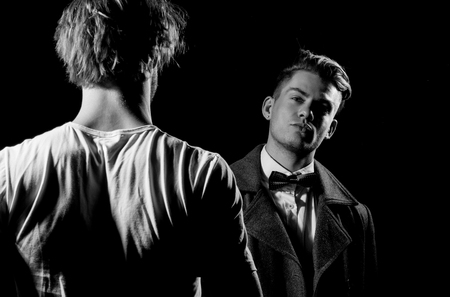 Two handsome men standing opposite on black background. businessman in classic bow tie, shirt and dark coat. Male model in white tshirt, casual wear. Fashion confrontationの写真素材