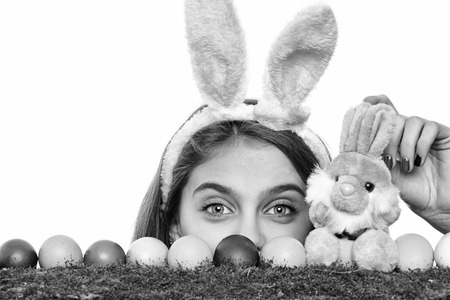 happy easter, traditional spring holiday celebration. girl in pink bunny ears with colorful painted eggs on green moss and rabbit toy, has smiling cute face isolated on white background, copy spaceの写真素材