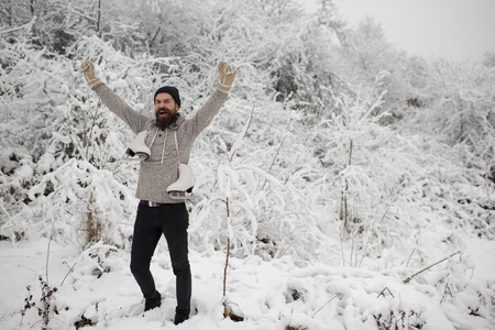 bearded man with happy face hold hand up with skate in snowy winter forest at christmas holiday, winter sport and rest, holiday and vacation, thermal pants, freezingの写真素材