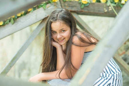 Happy childhood concept. Girl sit in greenhouse in spring or summer garden. Small child with long hair smile outdoor. Fashion, beauty, look, hairstyle. Floristry, horticulture, flower shop.の写真素材