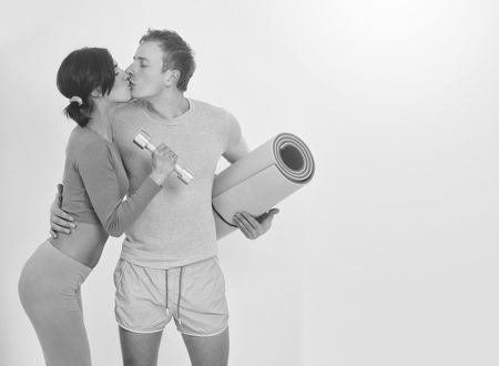 kissing couple in blue sportswear of pretty woman or cute girl with fitness mat and handsome guy man with muscular torso and sexy body training in sport gym with dumbbells isolated on white backgroundの写真素材