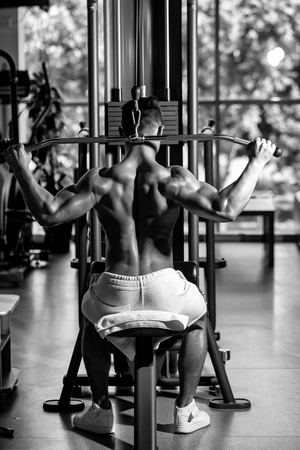 Handsome young man with sexy muscular wet body and bare back training with heavy exercise equipment in gymの写真素材