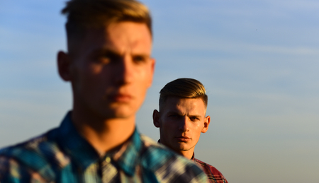 Young handsome caucasian twins in shirts look away with serious face on sky backgroundの写真素材