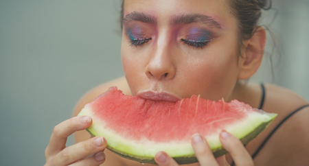 Young woman eat juicy watermelon. Girl with makeup face and red melon. Beauty, look, visage. Summer, fruit, harvest season. Food, diet, health. Vegetarian, organic, vitamin.の写真素材