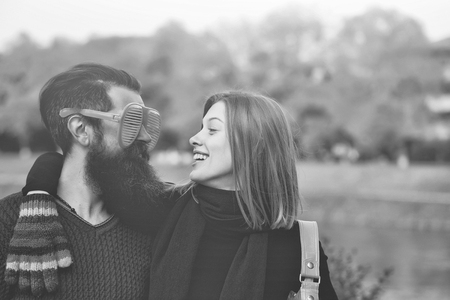 Young couple of pretty girl and bearded man hipster with funny orange eyeglasses outdoors in park on autumn day on natural backgroundの写真素材