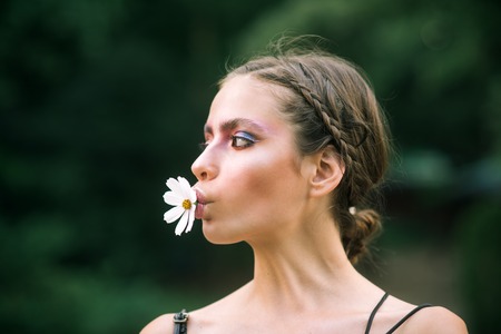 Woman with daisy flower in mouth. Health and beauty, eco, bio, nature concept. Spring, springtime, summer season. Fashion, look, makeup. Youth, flowering, blossom, bloom.の写真素材