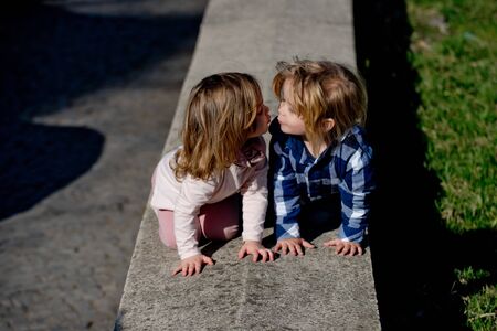 Boy and girl kiss on stone kerb on sunny day. Family, love, trust. Children, childhood concept.の写真素材