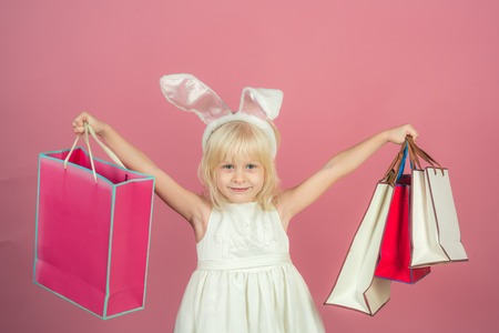 Small girl in bunny ears, easter. Child smile with with paper bags. Shop, shopping, sale. Kid fashion, beauty, look. Easter, spring holidays celebration, punchy pastel trendの写真素材