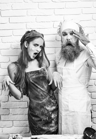 Messy pretty girl or beautiful woman and handsome man, cook or baker with flour on face, beard and moustache hug excited on white kitchen wallの写真素材