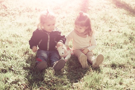 Sister and brother play with toy horse on sunny day. Girl and boy sit on green grass. Family, love, trust. Kids, friends, friendship. Children, childhood concept.の写真素材