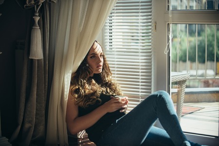 Beauty, fashion, look, makeup, hairstyle. Girl at window with cup of tea or coffee. Relax, comfort, lifestyle.の写真素材