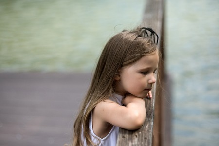 Girl child with long hair look at water from bridge. Summer vacation, adventure, discovery concept.の写真素材
