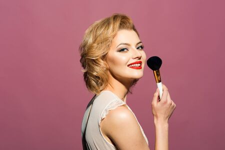 Cute pin up girl applying blusher on pink background
