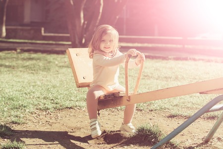 Girl smile on seesaw on sunny day. Child have fun on playground. Balance, equilibrium, harmony. Kid on teeter totter outdoor. Childhood, activity, lifestyle.の写真素材