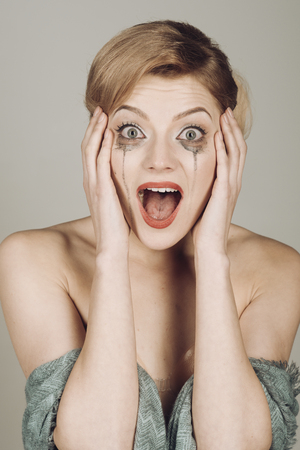 Girl cry with mascara streams on face. Lady with blonde hair and elegant hairstyle cry. Woman with shocked face with makeup on grey background. Drama and shock concept.の写真素材