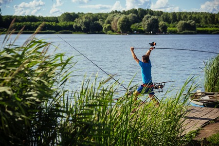 Spin fishing, angling, catching fish. Fisherman cast fishing rod in lake or river water. Man fish with spinning tackle on wooden pier. Adventure, sport, activity. Hobby, vacation, pastime.の写真素材