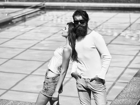 Young couple of stylish man and beautiful girl stand near swimming pool outdoor on sunny summer dayの写真素材