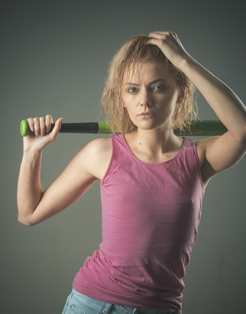 Girl with untidy hair holds bat on shoulder. Sportive lady or fitness trainer after training or...