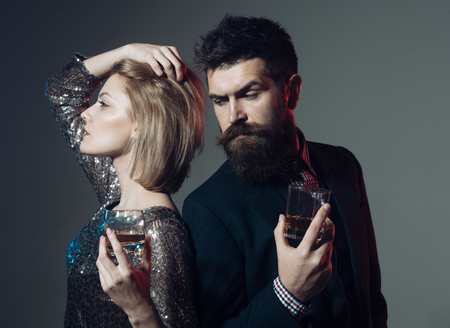 Quarrel and broke up concept. Couple stand back to back with wineglasses. Couple quarreled at corporate party. Desperate woman in fancy dress and man with strict face on grey background.の写真素材