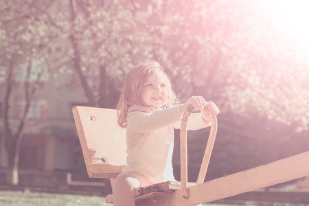 Happy childhood, activity, lifestyle. Girl smile on seesaw on sunny day. Balance, equilibrium, harmony. Kid on teeter totter outdoor. Child have fun on playground.の写真素材