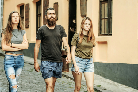 Friends walk on city street, vacation. Hipster with girlfriends, relations. Love triangle, cheating, lovers. Vacation, travel, trip. Friendship, friends, youth, relations. Summer fashion, styleの写真素材