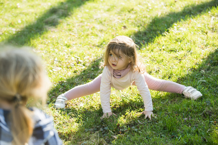 Girl split legs on green grass. Children play on sunny day outdoor. Activity, energy, lifestyle concept. Sport, yoga, pilates for kids.の写真素材