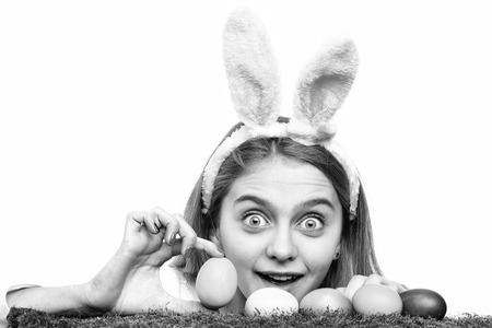 happy easter celebration and decoration. traditional spring holiday food. girl in pink bunny ears, colorful painted eggs on green moss, long blonde hair, surprised face isolated on white backgroundの写真素材
