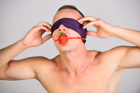 Man with tied eyes and strawberry in mouth, matriarchy. bdsm, erotic games, orgasm. man under domination, submission, oral sex, temptation. Love, relations, dominating. Sexshop, foreplay, diet.の写真素材