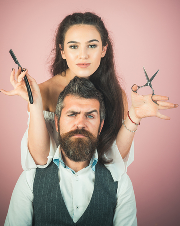 Happy positive woman and bearded man, hairdresser in the salon. Serious brutal man hairdresser making hairstyle for pretty woman in barber shop. Beautiful fashion coupleの写真素材