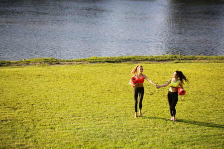 Two women walking with yoga mats outside on rural area wearing sports wear and doing yogaの写真素材
