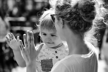 Mother young woman in sunglasses holds happy son baby boy with blonde hair in blue shirt sunny day outdoor in street on blurred backgroundの写真素材