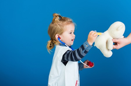 Boy cure toy pet with vaccine on blue background. Child make injection to teddy bear in mothers hand. Veterinary doctor game concept. Vaccination, health, healthcare, copy spaceの写真素材