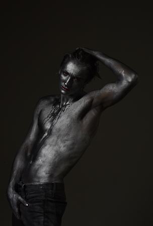 Shirtless man covered with shimmering silver paint, dark background. Fashion and masculinity concept. Macho with streams of sweat or paint on naked chest.の写真素材