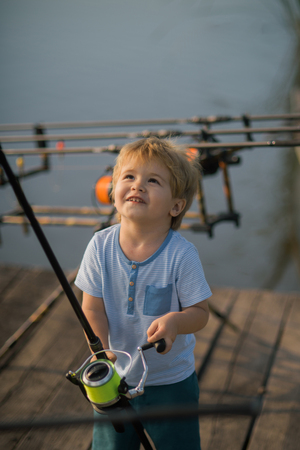 Fishing, angling, activity, adventure, sport. Child with fishing rod on wooden pier. Childhood, education, training. Summer vacation, hobby, lifestyle. Little boy learn to catch fish in lake or river.の写真素材