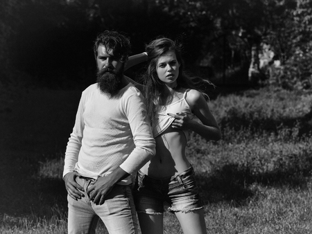 young couple of sexy woman with long blonde hair and bare belly with bearded handsome man with beard and stylish hairstyle standing in lawn with green grass sunny summer outdoorの写真素材