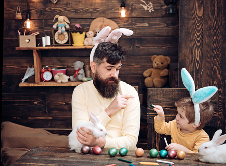 Easter family with fake bunny ears. Father and kid painting Easter eggs.の写真素材