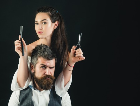 Young handsome man with long beard and moustache on serious face with young woman cutting with scissorsの写真素材