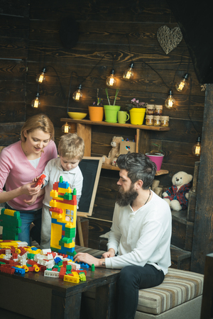 Family on busy face spend time together in playroom. Kid with parents play with plastic blocks, build construction. Father, mother and cute son play with constructor bricks. Educational game concept.の写真素材