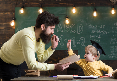 Father, teacher reading book, teaching kid, son, chalkboard on background. Dad wants to grow up genius son. Boy child in graduate cap likes to listening dad. Wunderkind and genius concept.の写真素材
