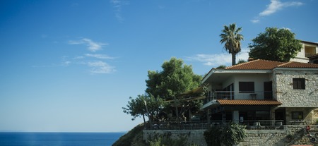 Luxury summer house on hilly sea coast. Building with garden, trees and palm tree. Villa near sea with blue sky on background on sunny day, copy space. Luxury life concept.のeditorial素材