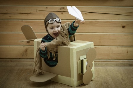 Young child pilot flying a cardboard box on wooden backgroundの写真素材