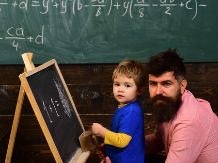Preschool kid and his teacher in the classroom. Father helping his little boy with math. Daddy hugging his kid.の写真素材