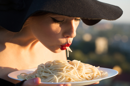 restaurant critic tatse italian pasta. restaurant, woman with red lips in black hat eating pasta.の写真素材