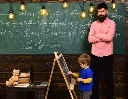 Strict math teacher checking pupil s work. Blond schoolboy solving equation at chalkboard. Preschool education concept.の写真素材