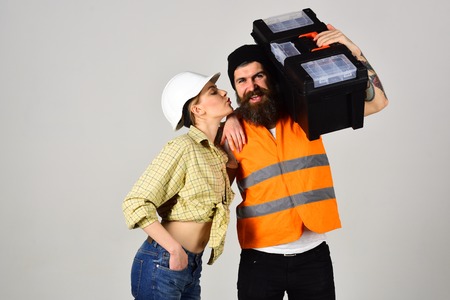 Housewife flirting with repairman with toolbox. Girl with helmet on kissing face near strong man...