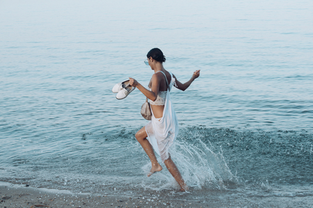 Young beautiful lady run on sea or ocean beach in water splashの写真素材