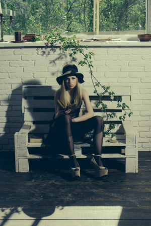 Poetry book at romantic writer. Fashion woman model read book. spring or summer girl relax on bench. Beauty and fashion look in vintage style. Pretty girl in black dress and retro hat.の写真素材